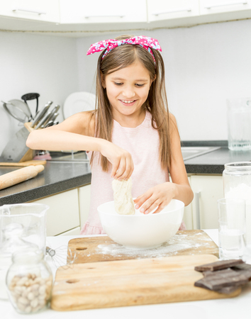 Beautiful little girl with pink bow on hair making dough on kitchen