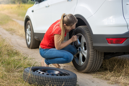 Young woman changing flat tire in fieldの写真素材