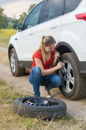 Woman unscrewing nuts on car flat wheel at fieldの写真素材