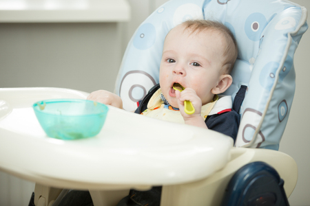 Cheerful smiling baby boy playing with spoon in highchairの写真素材