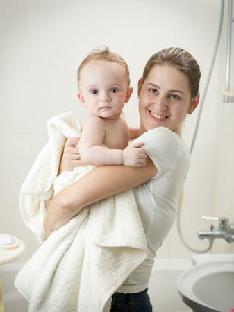 Young mother kissing her baby at bathroom after having bathの写真素材