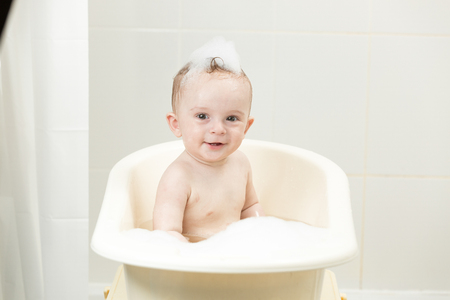 Cheerful smiling boy sitting in bath covered in foamの写真素材