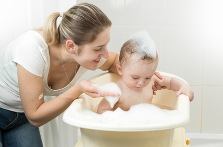 Portrait of smiling mother playing with baby in bathの写真素材