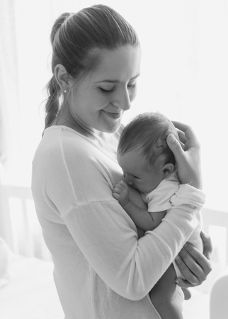 Monochrome portrait of beautiful young mother posing with her baby at child bedroomの写真素材