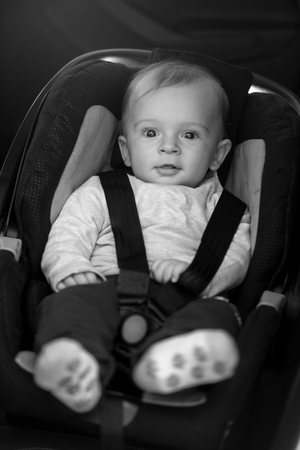 Black and white portrait of cute baby boy sitting in car safety seatの写真素材