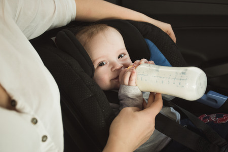 Portrait of baby boy drinking milk from bottle on car back seatの写真素材