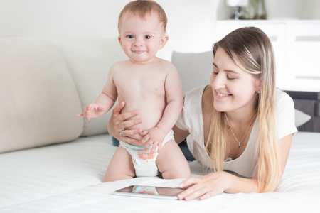 Smiling mother and baby boy using digital tablet on bedの写真素材