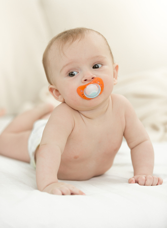 Cute baby with soother wearing diapers lying  on bedの写真素材