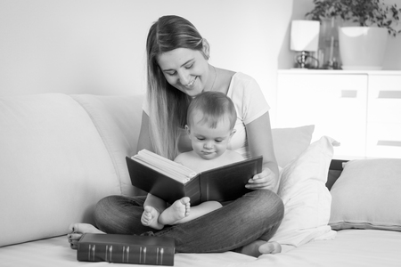 Black and white portrait of young mother reading book to her babyの写真素材