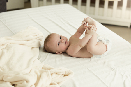 Little baby lying on bed and holding feetの写真素材