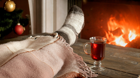 Closeup image of young woman in woolen socks lying under blanket next to burning fireplace with glass of mulled wineの写真素材