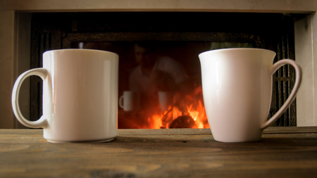 Closeup image of two cup of tea on wooden table next to burning fireplaceの写真素材