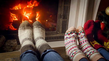 Closeup image family wearing knitted wool socks warming feet at fireplace next to decorated Christmas treeの写真素材