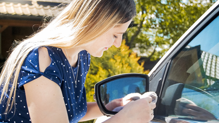 Young smiling woman wiping her car side mirrors with clothの写真素材
