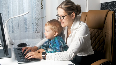 Beautiful young businesswoman working on computer with her 2 years old baby boyの写真素材