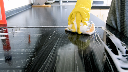 Closeup image of young woman in yellow latex gloves cleaning electric hob with sponge and foamの写真素材