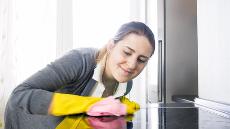 Beautiful smiling housewife cleaning stained glas surface of electric hobの写真素材