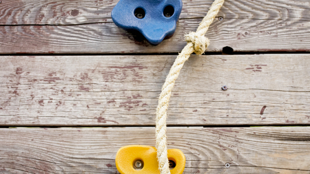 Closeup image of rocks for climbing and rope on wooden wall at children playground