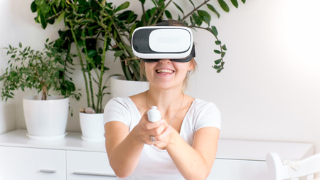 Portrait of laughing young woman playing video games in VR helmet