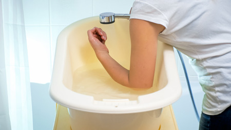 Closeup image of young woman checking water temperature in baby bathtub with elbowの写真素材