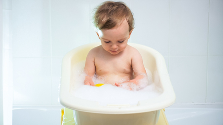 Cute adorable toddler boy bathing in small plastic bathtub