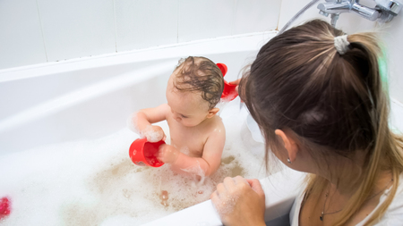 Young mother washing her toddler son in bathの写真素材