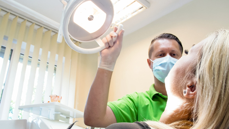 Portrait of dentist adjusting lamp and looking at young female patientの写真素材