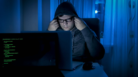 Portrait of male hacker working at night and wearing hood on head