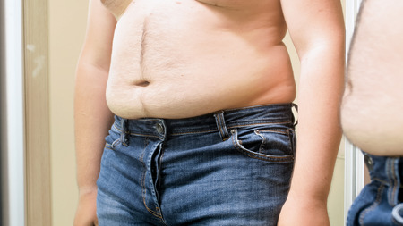 Closeup of young man with fat hairy tummy standing at mirrorの写真素材