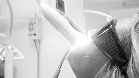 Black and white image of young woman sitting in dentist office during teeth whiteningの写真素材