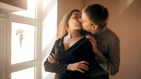 Toned portrait of beautiful young couple kissing at big windowの写真素材