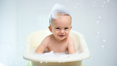 Portrait of cute smiling toddler boy sitting in bath with suds on head and flying soap bubblesの写真素材