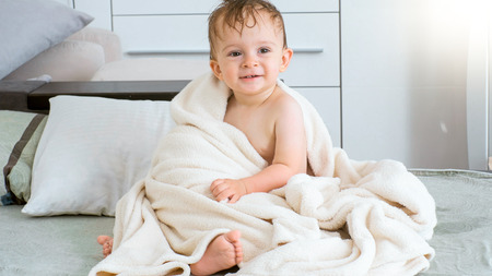 Portrait of cute smiling baby boy after bathing sitting on bedの写真素材