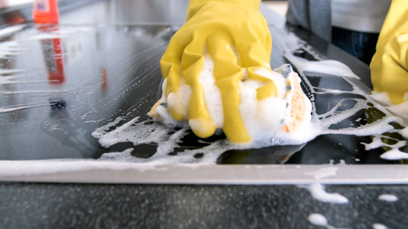 Closeup image of hand in yellow rubber glove holding sponge with sudsの写真素材