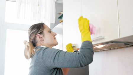 Portrait of young housewife washing kitchen wooden cupboardsの写真素材