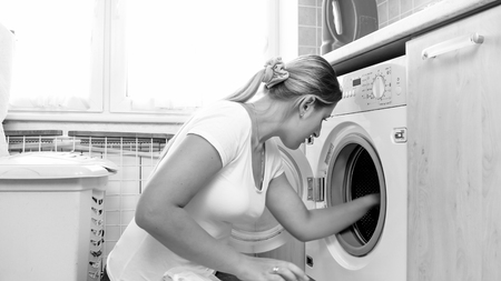 Black and white portrait of young woman taking clothes out of washing machineの写真素材