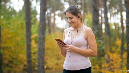 Portrait of smiling sporty woman using smartphone while running in forestの写真素材