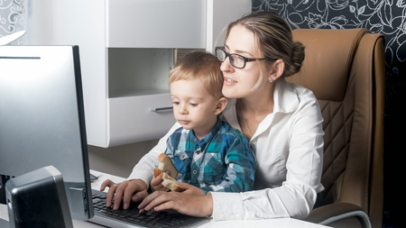 Portrait of adorable toddler boy eating while his mother working in officeの写真素材