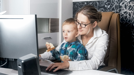 Cute 2 years old boy sitting in office with his motherの写真素材