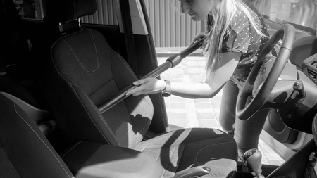 Black and white photo of young woman cleaning car seat with vacuum cleanerの写真素材