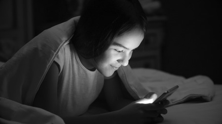 Black and white portrait of smiling girl lying in bed with mobile phoneの写真素材