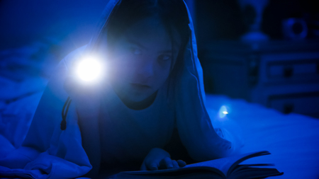 Portrait of girl lying in bed with flashlight at nightの写真素材
