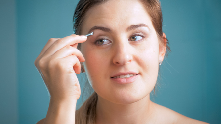 Closeup portrait of smiling brunette woman plucking eyebrows at mirrorの写真素材