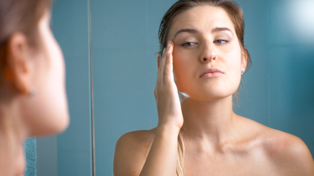Beautiful brunette woman checking her face for aging wrinkles in bathroomの写真素材