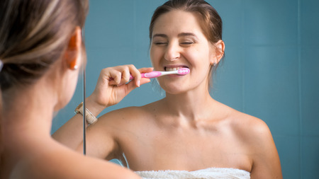 Photo of happy smiling woman cleaning teeth in morning at bathroomの写真素材