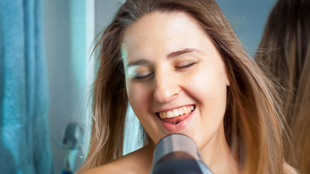 Happy smiling woman singing with hair dryer at bathroomの写真素材