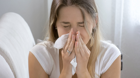 Closeup portrait of sneezing sick woman at homeの写真素材