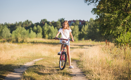 Toned image of beautiful smiling teenage girl posing on bicycle in fieldの写真素材