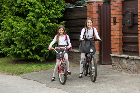 Two smiling girls in school uniform riding to school on bicyclesの写真素材