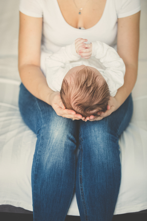 Toned closeup photo of young woman sitting on bed and holding her 3 months old babyの写真素材